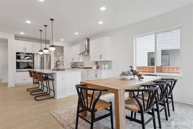 kitchen featuring a center island with sink, white cabinets, wall chimney exhaust hood, decorative light fixtures, and stainless steel appliances