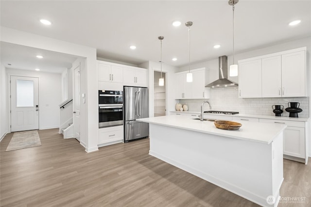 kitchen featuring backsplash, light countertops, appliances with stainless steel finishes, and wall chimney exhaust hood
