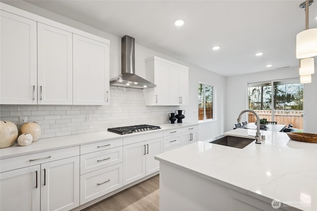 kitchen featuring recessed lighting, white cabinets, wall chimney exhaust hood, stainless steel gas stovetop, and a sink