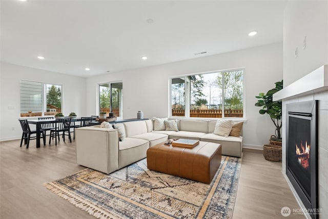 living area with recessed lighting, visible vents, light wood-type flooring, and a lit fireplace