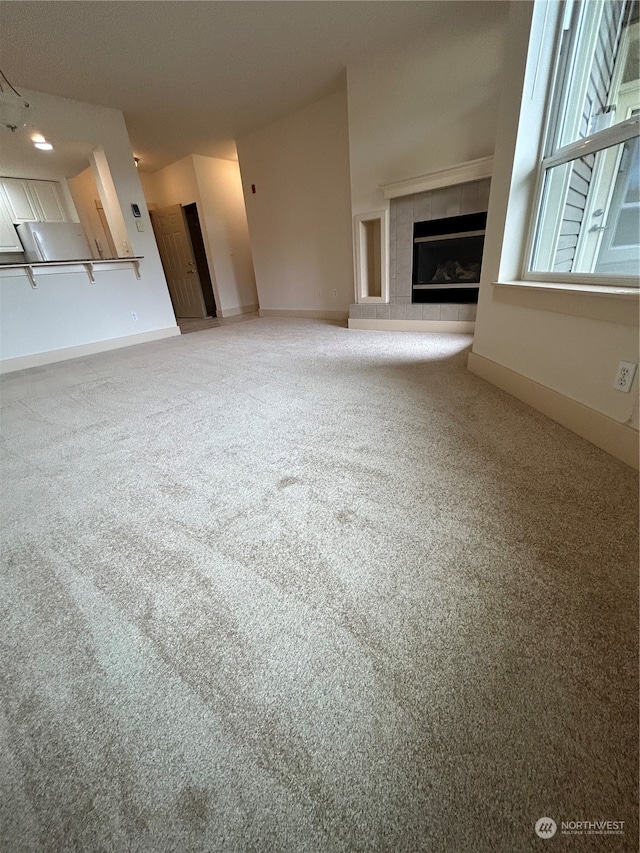 unfurnished living room with carpet floors and a tiled fireplace