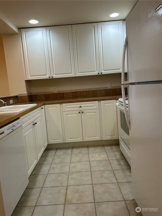 kitchen with white cabinetry, sink, light tile patterned flooring, and white appliances