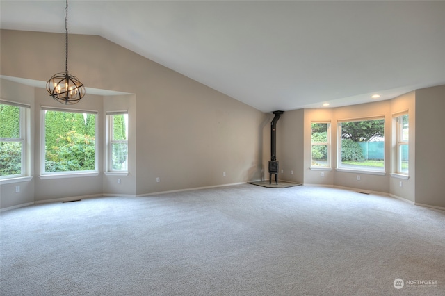 unfurnished living room featuring a wood stove, light colored carpet, a chandelier, and lofted ceiling