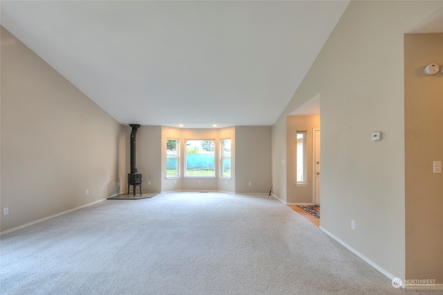 unfurnished living room featuring light colored carpet, a wood stove, and vaulted ceiling