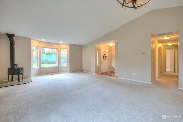 unfurnished living room featuring vaulted ceiling, light colored carpet, a wood stove, and a notable chandelier