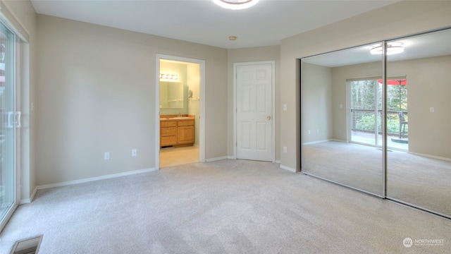 unfurnished bedroom featuring ensuite bath, light carpet, and a closet