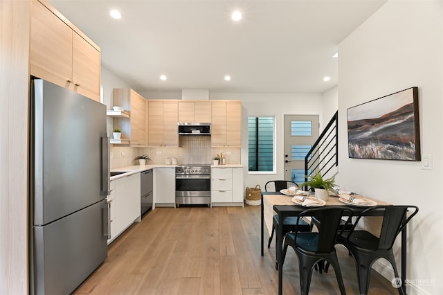 kitchen with light brown cabinets, stainless steel appliances, tasteful backsplash, and light hardwood / wood-style floors