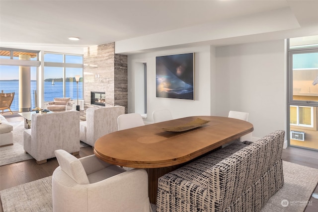 dining space with a fireplace, dark hardwood / wood-style flooring, a water view, and a wall of windows