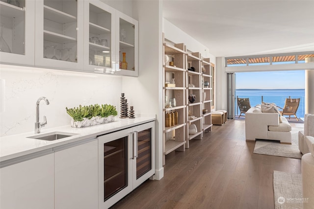 bar featuring dark hardwood / wood-style flooring, beverage cooler, sink, a water view, and white cabinetry