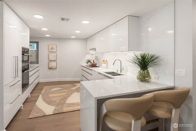 kitchen featuring kitchen peninsula, a kitchen breakfast bar, sink, light hardwood / wood-style floors, and white cabinetry