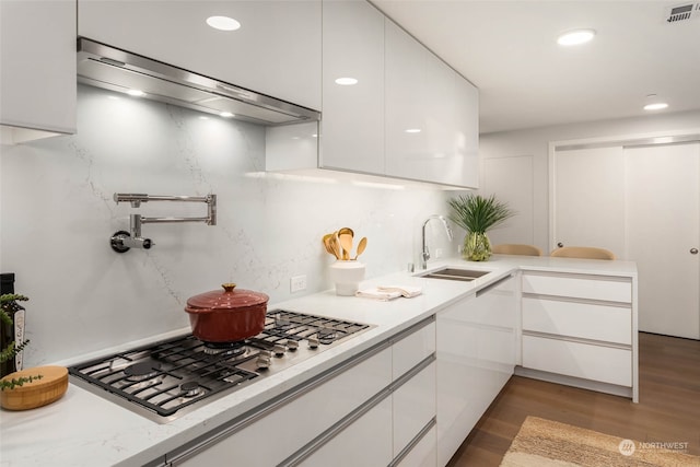 kitchen with stainless steel gas cooktop, sink, dark hardwood / wood-style floors, white cabinetry, and range hood