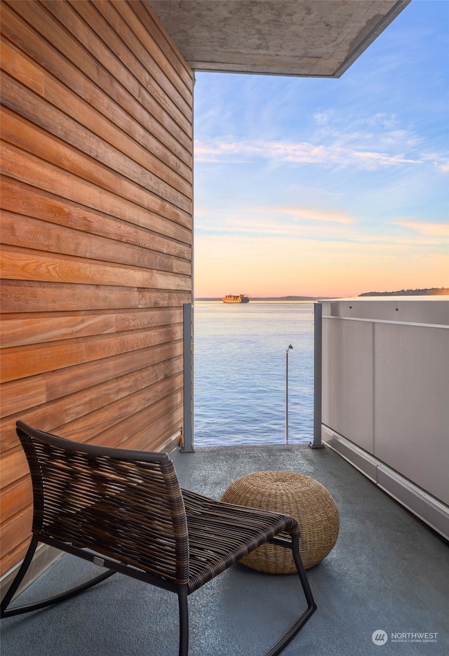 balcony at dusk featuring a water view