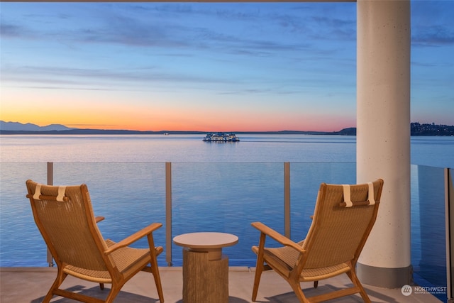 balcony at dusk featuring a water view