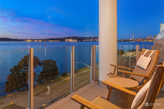 balcony at dusk featuring a water view