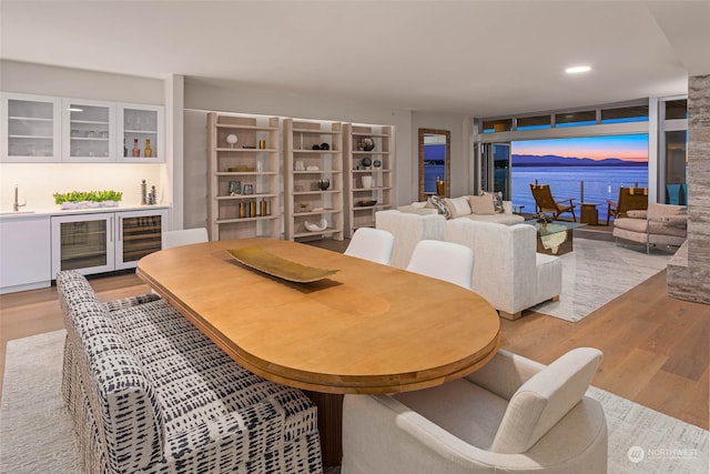 dining area featuring bar area, wine cooler, a water view, and light wood-type flooring