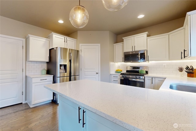 kitchen with backsplash, stainless steel appliances, pendant lighting, white cabinets, and light hardwood / wood-style floors