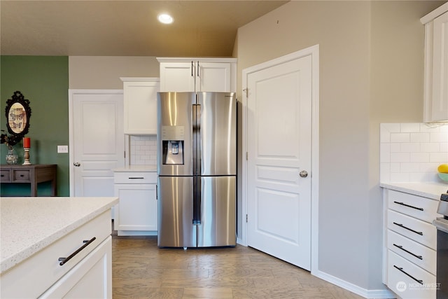 kitchen featuring backsplash, white cabinets, stainless steel fridge, light stone counters, and wood-type flooring