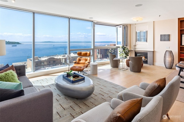 living room with floor to ceiling windows, a water view, and light hardwood / wood-style floors