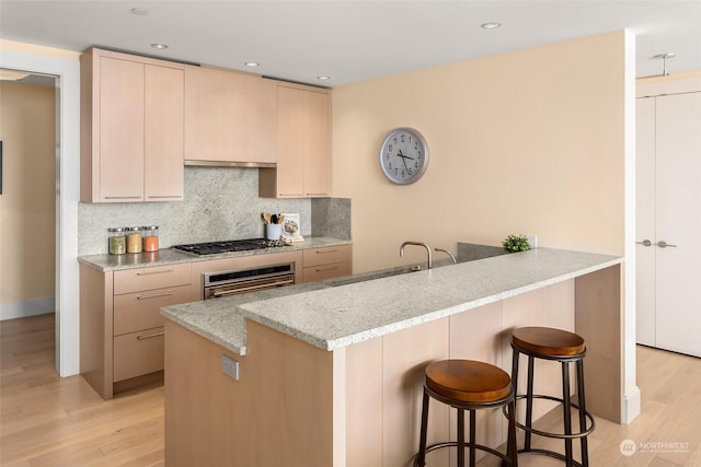 kitchen featuring kitchen peninsula, appliances with stainless steel finishes, light brown cabinetry, light stone counters, and light hardwood / wood-style flooring