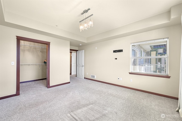 unfurnished bedroom with light carpet, a tray ceiling, a closet, and a chandelier