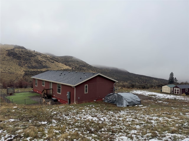 snow covered property featuring a mountain view and a storage shed