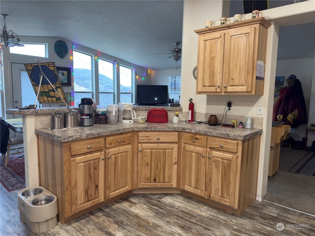 kitchen with ceiling fan with notable chandelier, dark hardwood / wood-style flooring, kitchen peninsula, and lofted ceiling