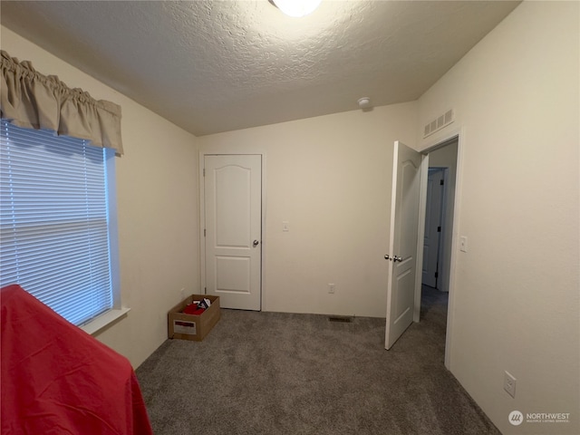 unfurnished bedroom featuring dark colored carpet, lofted ceiling, and a textured ceiling