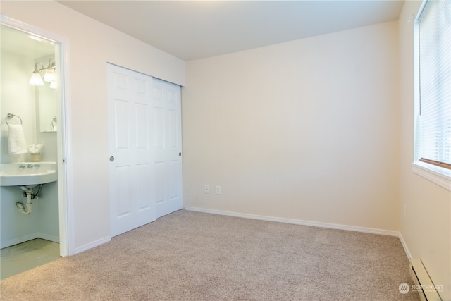 unfurnished bedroom featuring ensuite bathroom, a closet, light colored carpet, and a baseboard radiator