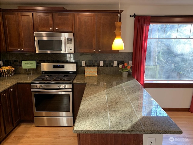 kitchen with light hardwood / wood-style flooring, decorative backsplash, appliances with stainless steel finishes, decorative light fixtures, and kitchen peninsula