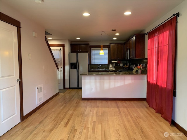 kitchen with sink, stainless steel refrigerator with ice dispenser, backsplash, pendant lighting, and light wood-type flooring