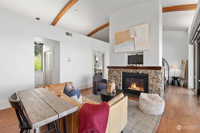 living room with vaulted ceiling with beams, hardwood / wood-style flooring, and a stone fireplace