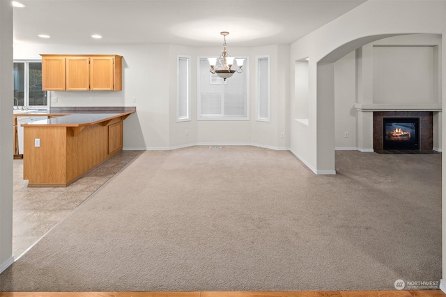 kitchen featuring a tile fireplace, hanging light fixtures, kitchen peninsula, a chandelier, and light carpet