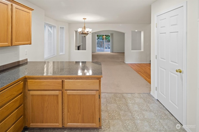 kitchen with a chandelier, light colored carpet, kitchen peninsula, and hanging light fixtures