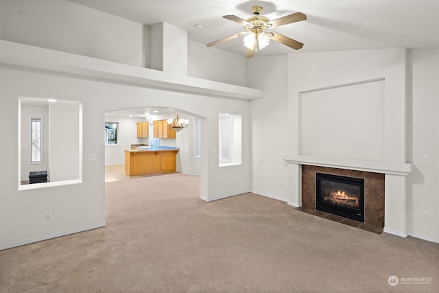 unfurnished living room with ceiling fan with notable chandelier, a healthy amount of sunlight, light carpet, and a tiled fireplace