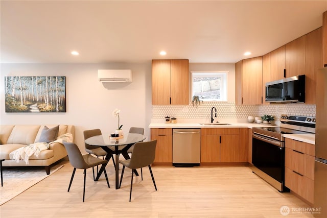 kitchen with light wood finished floors, light countertops, stainless steel appliances, an AC wall unit, and a sink