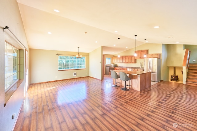 kitchen featuring lofted ceiling, a spacious island, hanging light fixtures, stainless steel fridge, and light wood-type flooring