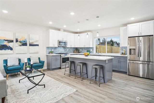 kitchen with a kitchen breakfast bar, hanging light fixtures, gray cabinets, light wood-type flooring, and appliances with stainless steel finishes