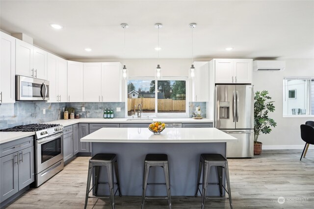 kitchen with gray cabinetry, a kitchen breakfast bar, hanging light fixtures, white cabinetry, and stainless steel appliances