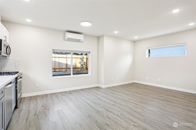 interior space with a wall mounted air conditioner, light hardwood / wood-style floors, stainless steel appliances, and a wealth of natural light