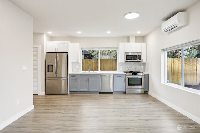 kitchen with light wood-type flooring, stainless steel appliances, an AC wall unit, and a wealth of natural light