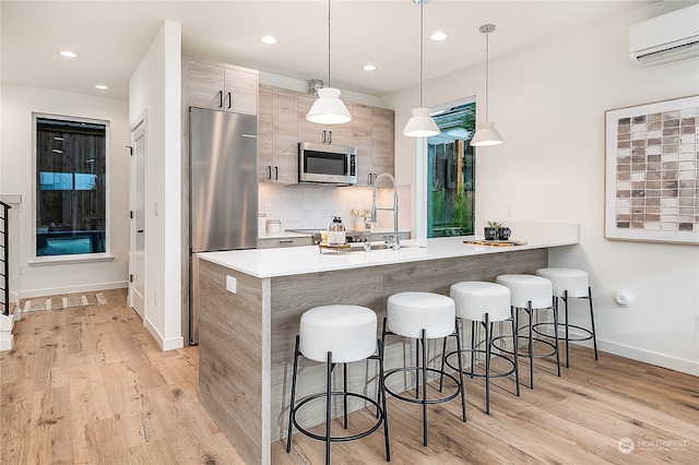 kitchen with hanging light fixtures, a kitchen breakfast bar, a wall mounted AC, appliances with stainless steel finishes, and light wood-type flooring