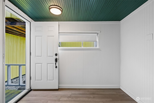 doorway to outside featuring light hardwood / wood-style flooring, crown molding, and wood walls