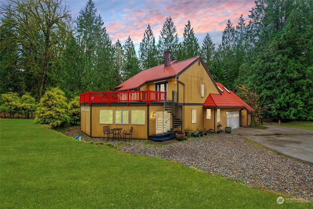 back house at dusk with a garage, a deck, and a lawn