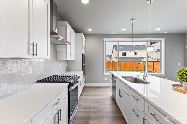 kitchen featuring wall chimney range hood, sink, stainless steel appliances, white cabinets, and decorative light fixtures