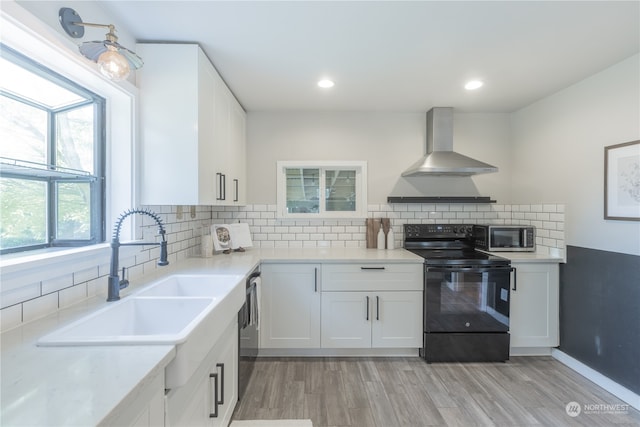 kitchen with black electric range, white cabinets, plenty of natural light, and wall chimney range hood