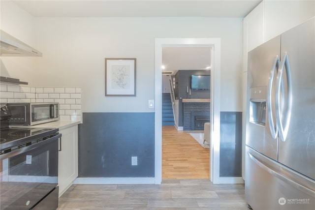 kitchen featuring white cabinets, a brick fireplace, appliances with stainless steel finishes, tasteful backsplash, and light hardwood / wood-style floors