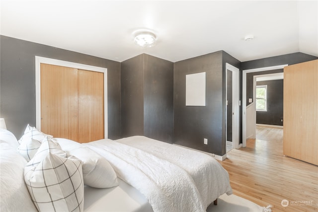 bedroom with light wood-type flooring, a closet, and lofted ceiling