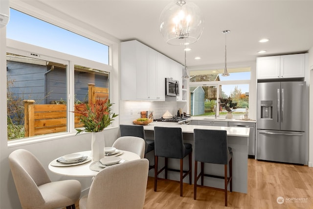 kitchen featuring pendant lighting, stainless steel appliances, white cabinetry, and a healthy amount of sunlight