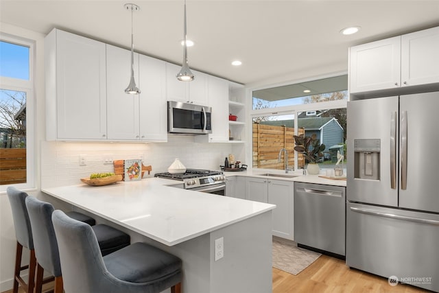 kitchen with white cabinetry, sink, stainless steel appliances, light hardwood / wood-style flooring, and kitchen peninsula