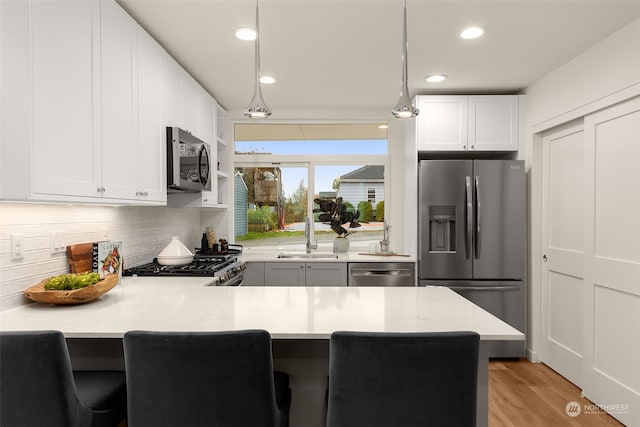 kitchen featuring kitchen peninsula, decorative light fixtures, light wood-type flooring, and stainless steel appliances